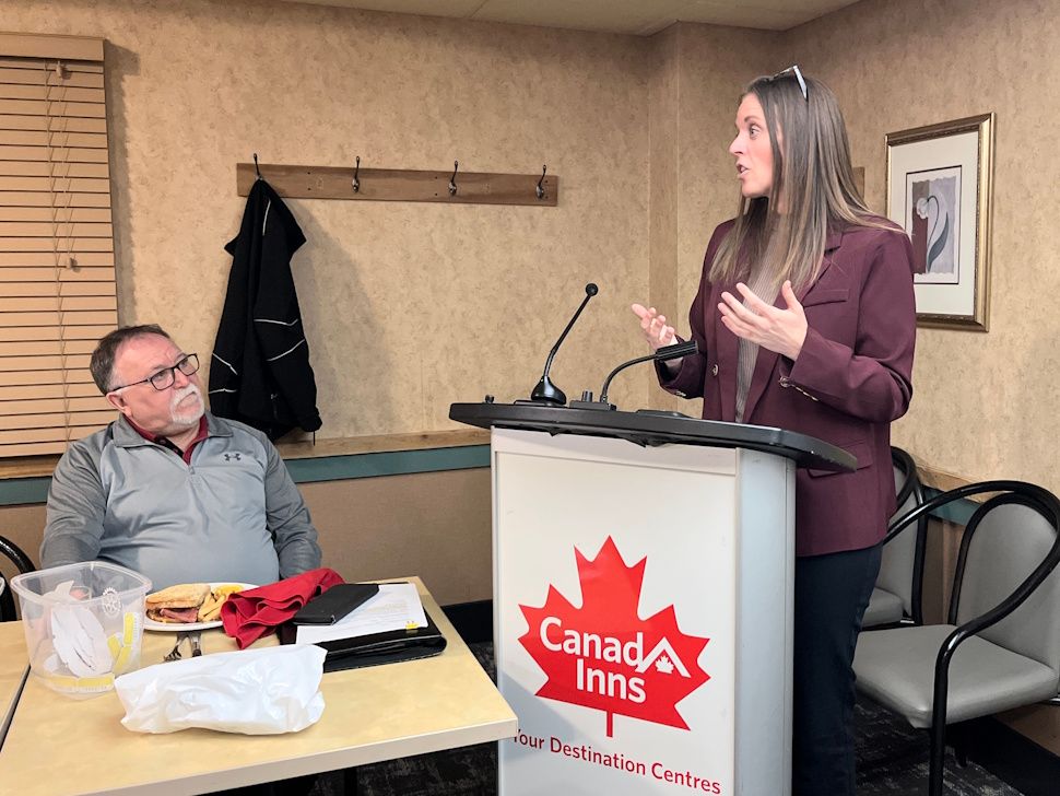 Tara Pettinger speaking at a Rotary meeting at Canad Inns in Portage la Prairie on May 5, with Rotary president Dave Roberts seated nearby listening.